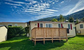 A cozy mobile home on a meadow, surrounded by trees. The sky is blue with interesting cloud formations.
