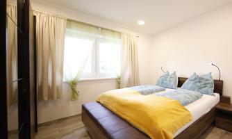 A cozy bedroom with a large bed and colorful pillows. Bright curtains let in plenty of daylight.