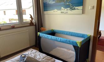 A cozy bedroom with a travel cot and a decorative wall mural. The room feels inviting and bright due to the daylight.