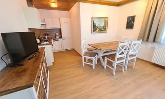 A bright and modern kitchen with a dining area. The room has wooden floors and large windows that let in a lot of light.
