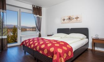 A cozy bedroom with a large bed and a red bedspread. The room has a window with a view of the countryside and is bright and inviting.