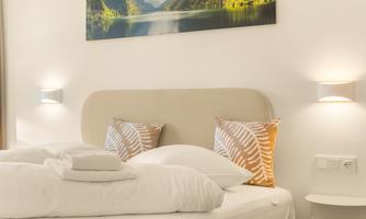 A cozy bedroom with a large bed and decorative pillows. A beautiful landscape picture of mountains and a clear lake hangs on the wall.