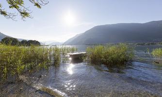 A beautiful lake with clear water and gentle waves. In the background, there are mountains and a shining sun.