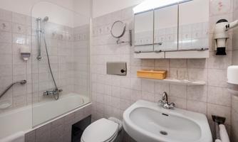 A small bathroom with a bathtub, shower, and sink. The walls are brightly tiled and well equipped.