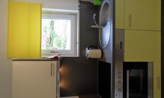 A modern kitchen with yellow and gray elements. It includes a stove, a sink, and a window with yellow curtains.