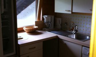 A bright kitchen setup with wooden details and large windows. On the countertop, there is a fruit bowl and kitchen appliances.