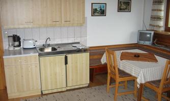 A cozy kitchen with wood-colored cabinets and a small dining table. The amenities include a refrigerator, a sink, and a coffee machine.