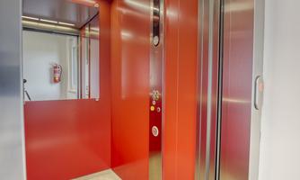 A modern elevator with red interior design. The floor is gray and there are mirrors on the walls.
