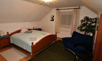 A cozy bedroom with a large bed and a blue armchair. The walls are light and a window provides daylight.