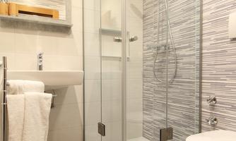 A modern bathroom with a glass shower cubicle and an elegant sink arrangement. The walls are designed with modern tiles in soft shades of gray.