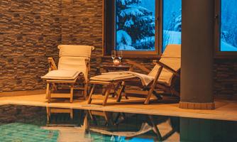A relaxing wellness area with two loungers and a pool. In the background, there are snow-covered trees and a tranquil atmosphere.