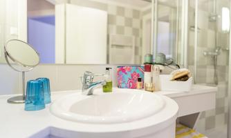 A modern bathroom with a round sink and a large mirror. On the shelf, there are care products and colorful glasses.