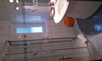 A bathroom with a shower cabin and a sink. The walls are tiled and there is a window for ventilation.
