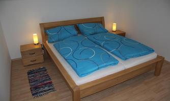 A modern bedroom with a large double bed and blue bedding. Next to the bed, there are two nightstands with lamps.