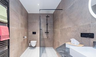 A modern bathroom with a glass shower enclosure. The walls are in neutral tones, and fresh towels as well as a sink are visible.