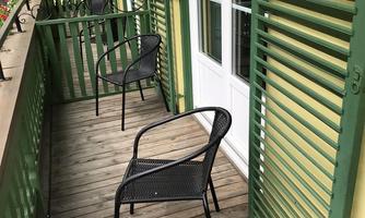 A balcony with a wooden floor and green shutters. Two black chairs are ready for a relaxed break.