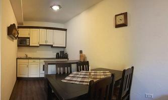 A cozy kitchen with a dining area. The table is set with a checkered cloth, and there are modern kitchen cabinets.