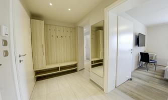 A modern hallway with a wardrobe and a large mirror. In the background, a television and a table can be seen.