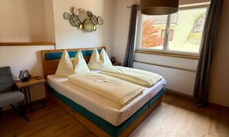 A cozy bedroom with a large bed and two pillows. The wooden floor and ceiling create a warm atmosphere.