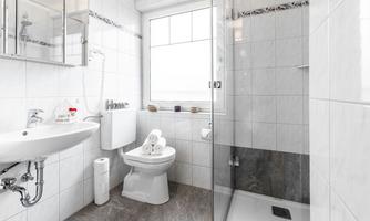 A modern bathroom with white tiles and a shower. The sink and toilet are clean and well arranged.