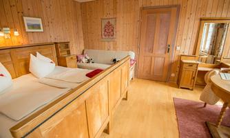 A cozy room with wooden-paneled walls and a double bed. The room is bright and friendly, with a small table and a mirror.