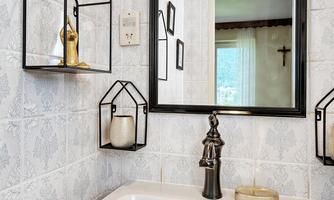 A modern bathroom with a white sink and a stylish mirror. Decorative shelves in the shape of houses hang on the wall.