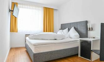 A modern room with a large bed and a television. Bright curtains let in a lot of light.