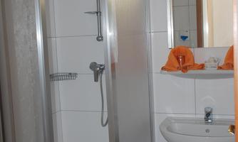 A simple bathroom with a shower cabin and a sink. White tiles and a mirror are mounted on the wall.