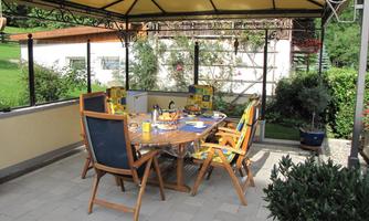 A cozy dining area under a pavilion. The table is set and surrounded by chairs, overlooking a green landscape.