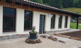 A modern building with an entrance and large windows. In front of the house, there is a rock garden with a flower pot.