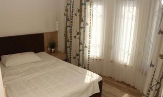 A bright, cozy bedroom with a single bed and large windows. The curtains are light and airy, and the room feels inviting and tidy.