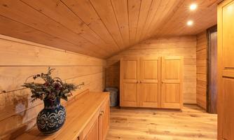 A cozy room with wooden paneling and warm light. On the dresser, there is a flower vase and there is a wardrobe against the wall.