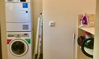 A laundry room with a washing machine and a dryer. On the wall are an ironing board and cleaning supplies.