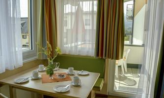 A cozy dining area with a table set for four people. Large windows let in plenty of light and provide access to a balcony.