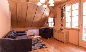 A cozy room with a wooden ceiling and wooden floor. There is a sofa, two armchairs, and large windows that provide plenty of light.