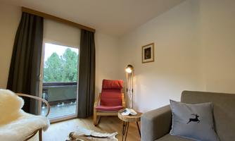A cozy living space with a red chair and a gray couch. The window offers a view of green trees outside.