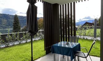 A beautiful outdoor area with a table and chairs under a canopy. In the background, mountains and a green meadow can be seen.
