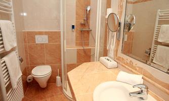 A modern bathroom with a shower, sink, and toilet. The walls are light tiled and equipped with towels.