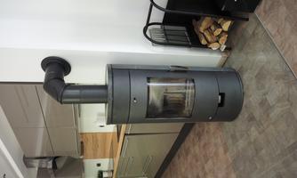 A modern fireplace stove in a stylish kitchen. The stove is black and offers a view of the fire through a glass front.