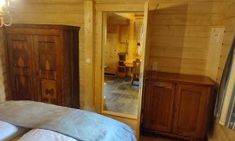 A cozy bedroom with wood paneling and a large mirror. In the background, a chair and a table can be seen.