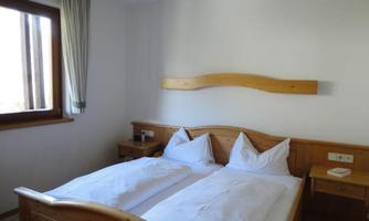A cozy bedroom with a wooden double bed. There is a window with curtains and a bedside table next to the bed.
