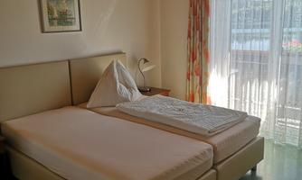 A simple bedroom with two beds and a large window. The room has a bright and friendly atmosphere.