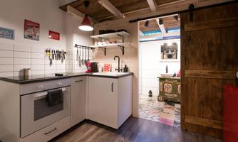 A modern kitchen with a wooden ceiling and colorful flooring. It is well-equipped and has plenty of natural light.