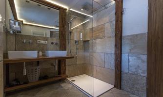 A modern bathroom with a glass shower and two sinks. The walls are designed with elegant tiles and wood paneling.