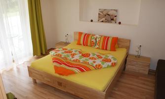 A cozy bedroom with a large yellow bed and colorful pillows. The walls are bright, and there are long curtains that let in plenty of light.