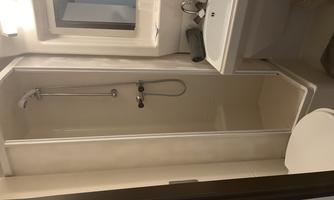 A small bathroom with a shower, sink, and toilet. The walls are light, and there is a mirror above the sink.
