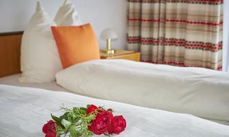 A cozy bedroom with two beds and elegant pillows. A decoration of red roses and fresh greenery lies on the bedspread.