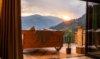 A cozy room with wooden floors and a view of the mountains. The sunset creates a warm atmosphere through the window.
