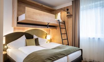 A modern bedroom with a double bed and a loft bed. The walls are done in light wood, and the room has large windows with curtains.