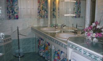 A modern bathroom with two sinks and a large mirror light. Colorful window curtains and a washing machine are also visible.